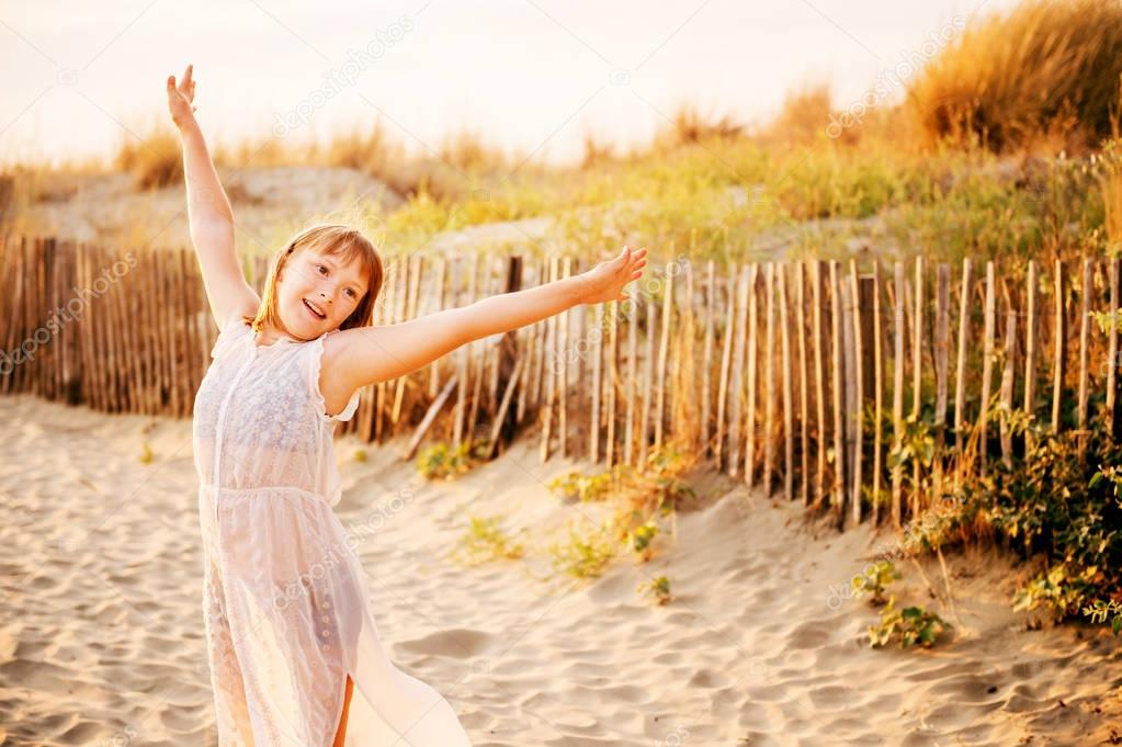 Beautiful kid girl dancing on sand beach by the sea at sunset. Preteen child enjoying summer vacation on south of France