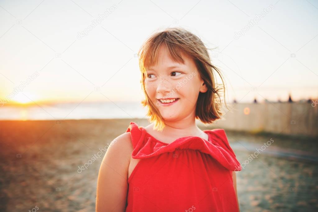 Close up portrait of sweet little girl with short bob haircut resting by the sea at sunset