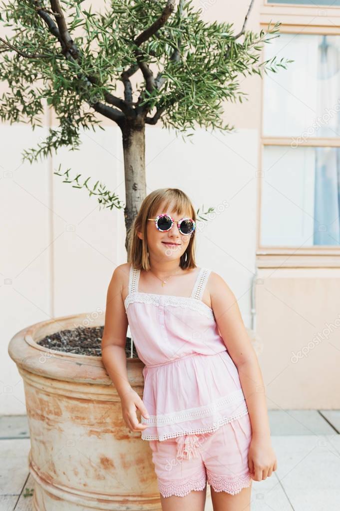 Outdoor portrait of adorable preteen kid girl wearing fashion pink top and shorts, walking on the streets of Provence, France
