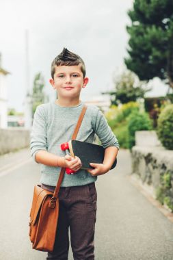 Açık kahverengi deri çanta omuz üzerinden giyiyor, kaykay tutan komik küçük okullu çocuk portresi. Geri okul kavramı. Film bak tonlu görüntü