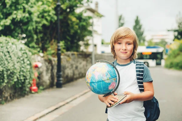 Ritratto all'aperto di ragazzino divertente che indossa lo zaino e tiene il mondo globo. Torniamo al concetto di scuola. Film immagine del filtro look — Foto Stock
