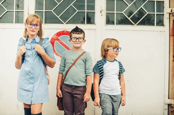Ομάδα τρία αστεία παιδιά φορούν σακίδια περπάτημα πίσω στο σχολείο. Κορίτσι και αγόρια που φορούν γυαλιά θέτοντας σε εξωτερικούς χώρους — Φωτογραφία Αρχείου