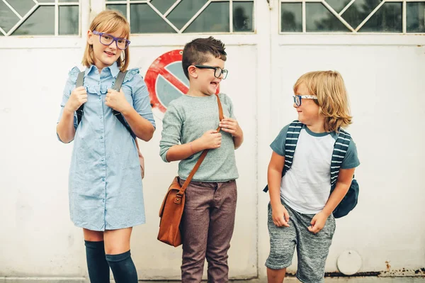 Group of three funny kids wearing backpacks walking back to school. Girl and boys wearing eyeglasses posing outdoors — Stock Photo, Image