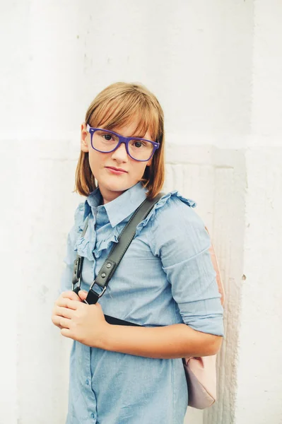 Außenporträt eines netten kleinen 9-10 jährigen Mädchens, das blaues Uniformkleid, Rucksack und Brille trägt. zurück zum Schulkonzept — Stockfoto