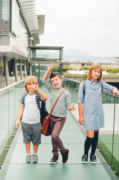 Grupo de 3 escolares divertidos posando al aire libre, usando mochilas. De vuelta al concepto escolar. Moda para niños —  Fotos de Stock