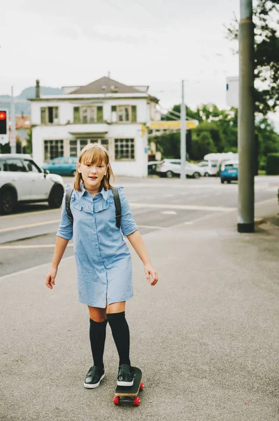 Funny little schoolgirl riding skateboard outside, back to school concept, film look toned image — Stock Photo, Image