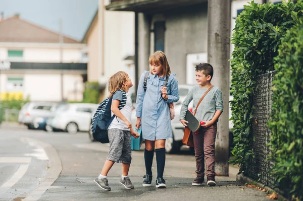 Grupo de 3 escolares divertidos caminando juntos de regreso a la escuela, usando mochilas, sosteniendo la lonchera y el monopatín —  Fotos de Stock