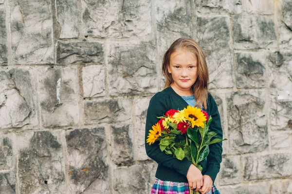 Outdoor portrait of a cute little girl wearing schoolwear, holding beautiful bouquet of autumn flowers — Stock Photo, Image