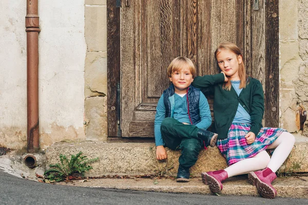 Grupa dwóch stylowe dzieci pozowanie na zewnątrz, odpoczynku obok Starego rocznika drzwi. Moda dla schoolkids. Obuwie i odzież dla szkoły. Mały chłopiec i dziewczynka gra razem — Zdjęcie stockowe