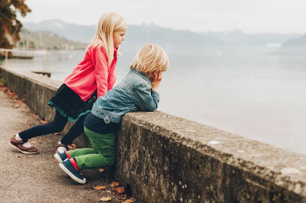 Deux enfants drôles profitant d'une belle et chaude journée d'automne près du lac Léman. Petit frère et grande sœur passent du temps ensemble dehors — Photo