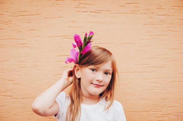 Retrato sincero de adorável menina de 6-7 anos segurando flor rosa ao lado da cabeça — Fotografia de Stock