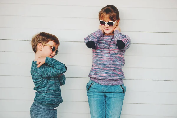 Group of two funny kids playing together outside, little boy and girl posing against white wooden background, brother and sister wearing matching pullovers, fashion for children, knitwear. — Stock Photo, Image