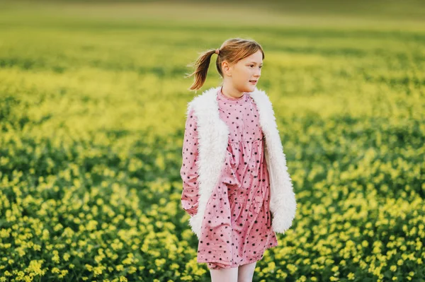 Plenerowej dość 10-letniej dziewczynki, sobie różowy sukienka vintage i kamizelka ze sztucznego futra, pozowanie na polu, ramiona skrzyżowanymi — Zdjęcie stockowe