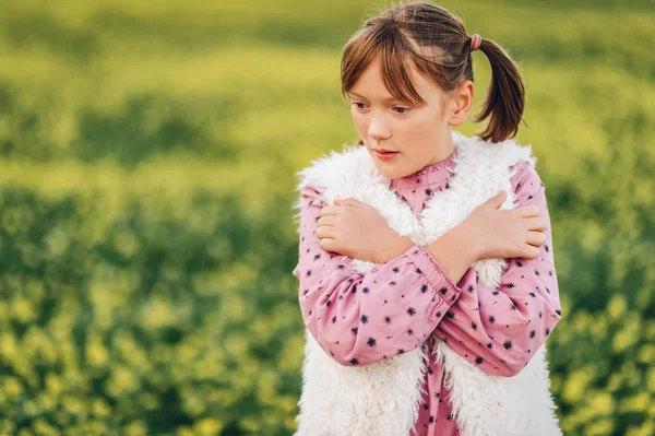 Plenerowej dość 10-letniej dziewczynki, sobie różowy sukienka vintage i kamizelka ze sztucznego futra, pozowanie na polu, ramiona skrzyżowanymi — Zdjęcie stockowe