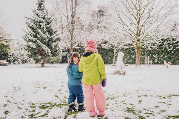 Dvě rozkošné děti spolu hrají ve Snowparku, teplé zimní oblečení, pohled zezadu — Stock fotografie