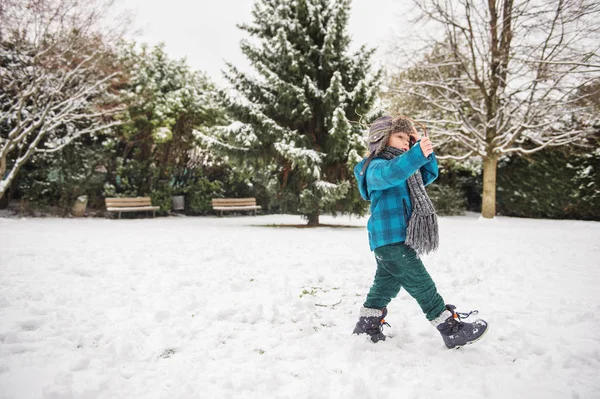 Schattige kleine jongen spelen in winter park. Kind buiten plezier, zittend op de sneeuw, het dragen van warme blauwe jas, muts en sjaal — Stockfoto