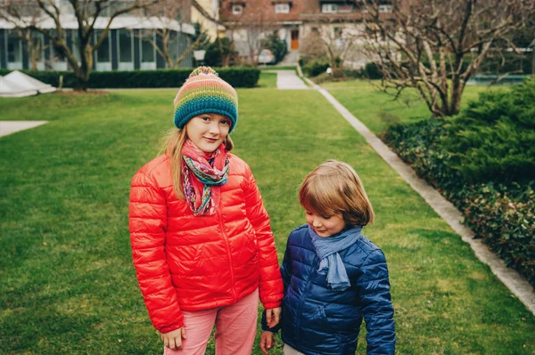 Two funny kids playing together in the park on a cold day, wearing warm padded jackets — Stock Photo, Image