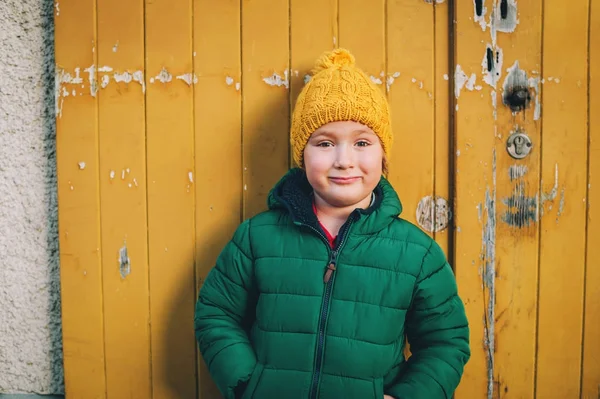 Outdoor portrait of a funny 4-5 year old little boy wearing green winter padded jacket and yellow hat — Stock Photo, Image