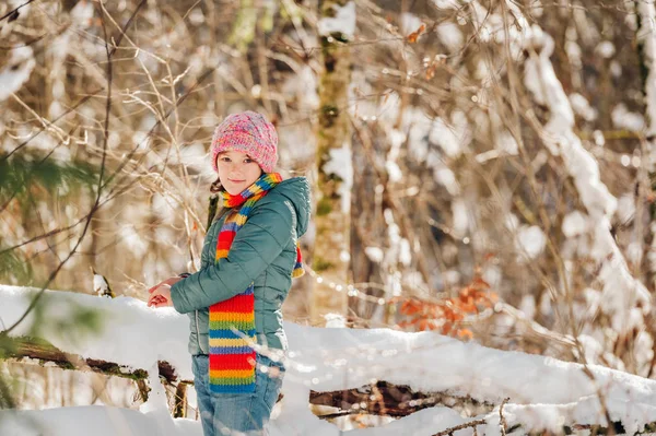 Utomhus porträtt av vackra lilla flicka som leker i vinter skog, bär färgglada halsduk och hatt — Stockfoto