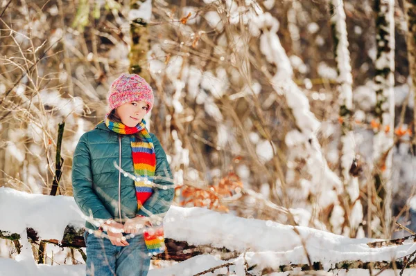 Retrato ao ar livre de menina bonita brincando na floresta de inverno, vestindo lenço colorido e chapéu — Fotografia de Stock