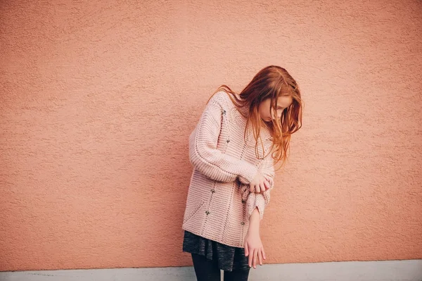 Außenporträt eines entzückenden rothaarigen Mädchens mit weichem rosa Pullover, das Kindermodel posiert vor beigem Wandhintergrund. Mode für junge Teenager — Stockfoto