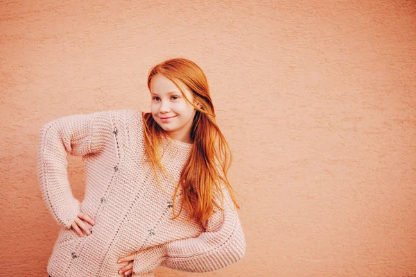 Outdoor Portret van schattige roodharige preteen meisje dragen van zachte roze trui, kid model poseren tegen beige muur achtergrond. Mode voor jonge tieners — Stockfoto