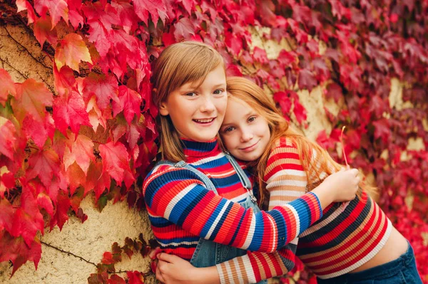 Autumn portrait of two funny girls playing together outside, posing against red ivy wall. Fall fashion for teens — Stock Photo, Image