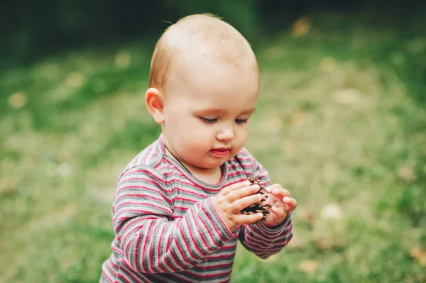 Adorável bebê menina de 9-12 meses de idade brincando com pinho cone fora — Fotografia de Stock