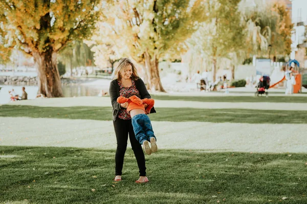 Joyeux jeune mère jouant avec un tout-petit garçon dans un beau parc ensoleillé par une journée chaude d'automne. Femme ayant du bon temps avec un fils — Photo