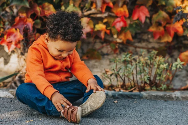 Retrato de adorável menino criança africana brincando ao ar livre em um belo dia de outono, vestindo jaqueta com capuz laranja brilhante — Fotografia de Stock
