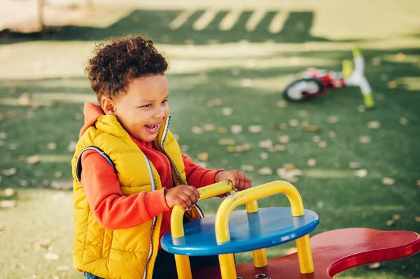 Adorável pequeno menino criança de 1-2 anos de idade se divertindo no parque infantil, criança vestindo casaco com capuz laranja e colete amarelo — Fotografia de Stock