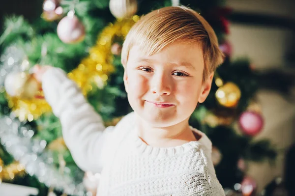 Feche o retrato do menino feliz brincando ao lado da árvore de Natal, vestindo pulôver quente branco — Fotografia de Stock