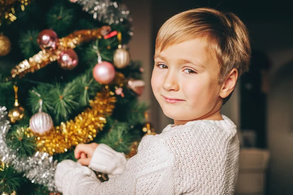 Feche o retrato do menino feliz brincando ao lado da árvore de Natal, vestindo pulôver quente branco — Fotografia de Stock
