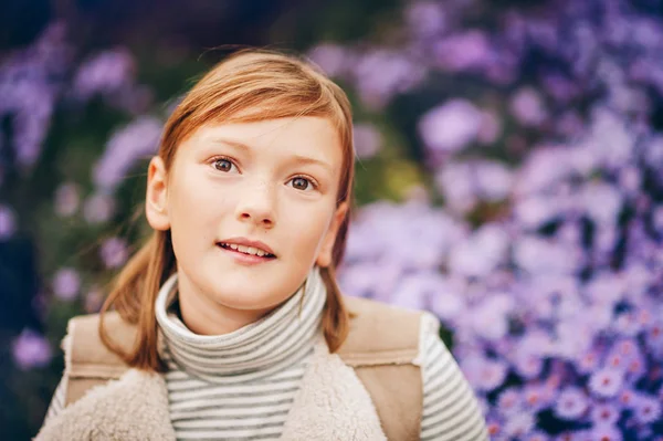 Openhartig portret van een lief klein meisje, bovenaanzicht, paarse bloemen achtergrond — Stockfoto