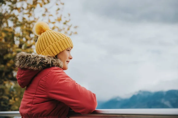 Portrait extérieur de jolie petite fille profitant d'une journée fraîche à l'extérieur, portant un chapeau jaune chaud et une veste d'hiver rouge — Photo