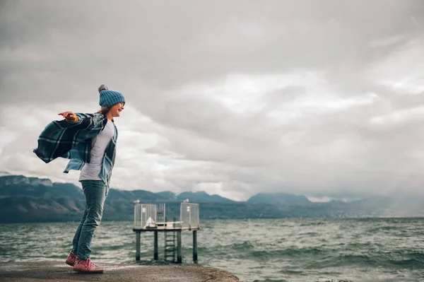 달콤한 작은 소녀는 매우 바람이 부는 날에는 호수 재생 블루 모자와 격자 무늬 판 쵸를 입고. 호수 제네바, 로잔, 스위스에서 촬영 이미지 — 스톡 사진