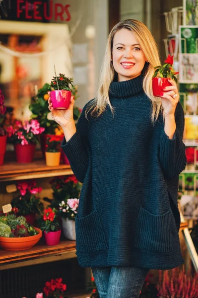Mujer feliz eligiendo pequeños regalos en la tienda de flores, usando jersey azul oscuro cálido —  Fotos de Stock
