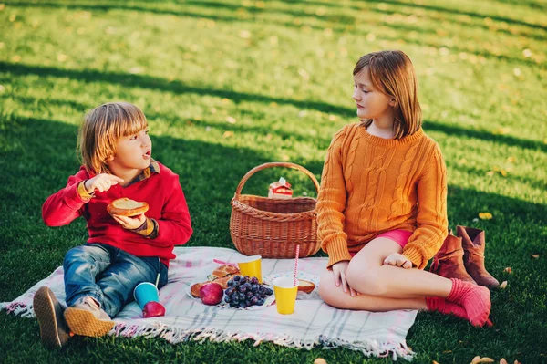 Děti, které jedí občerstvení venku. Děti spočívající v parku na pěkný slunečný den, sedí na deku — Stock fotografie