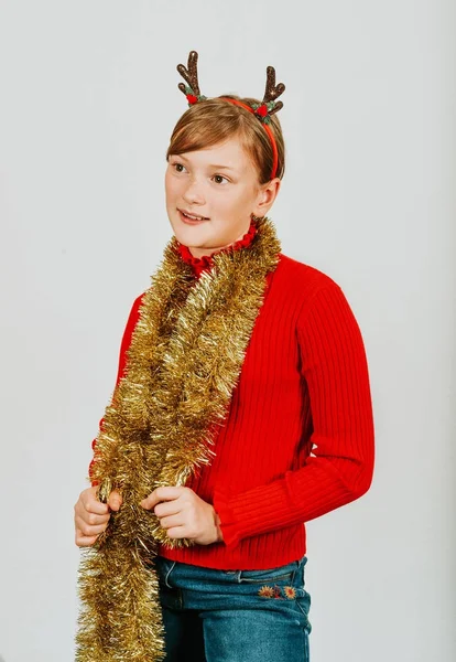 Retrato de Natal de menina bonito contra fundo branco, vestindo pulôver vermelho, orelhas de rena e guirlanda dourada — Fotografia de Stock