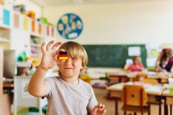 Menino bonito trabalhando em sala de aula, segurando bandeira alemã auto-feita, educação primária — Fotografia de Stock