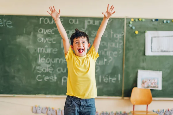 Criança feliz trabalhando em sala de aula, mãos levantadas, educação, de volta ao conceito de escola — Fotografia de Stock