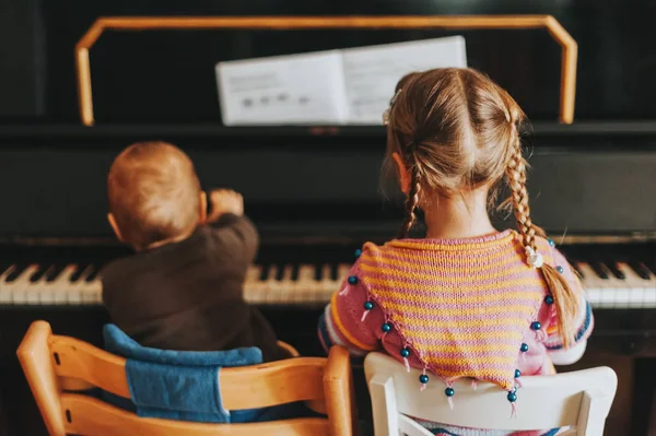 ピアノで遊ぶ二人の小さな子供幼児女の子と赤ちゃん 男の子の練習音楽家で 背面図 — ストック写真