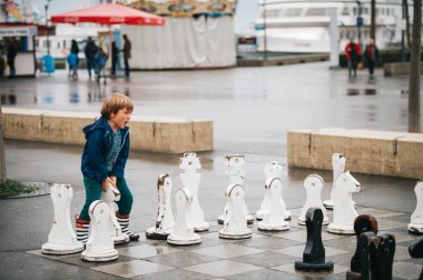 Yağmur ceket ve çizmeler giyen çocuk çocuk oyun, dev satranç oynuyor. Resim çekilen sıksam, Lausanne, İsviçre