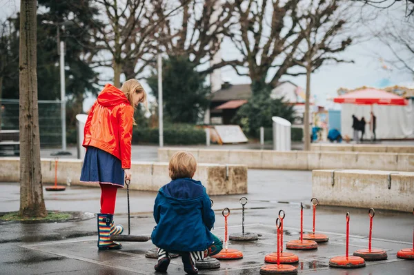 Grup iki Çocuk Bahçesi üzerinde dev dama oynarken yağmur paltolar ve botlar giyiyor. Resim çekilen sıksam, Lausanne, İsviçre