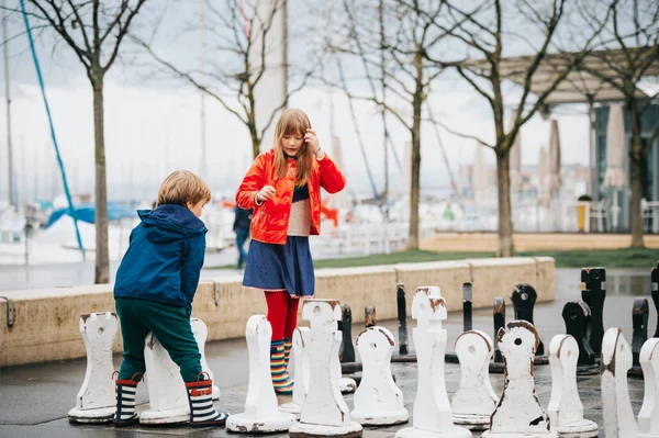 两个孩子在操场上玩巨型象棋 穿着雨衣和靴子 瑞士洛桑 Ouchy 的照片 — 图库照片