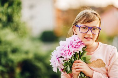 Açık tutarak taze pembe peonies güzel buket gözlük, giyen bir sevimli küçük 9 yaşındaki kız portresi