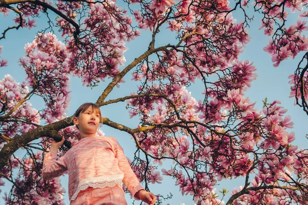 夕暮れの春の花は木蓮で遊んで ピンクのトレーナーを着て喜んでいる子供女の子 — ストック写真