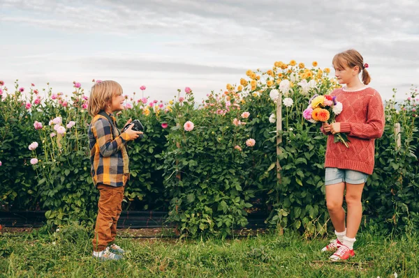 つの面白い子供たち美しい菊の庭で一緒に遊んで かわいい妹の写真を撮るカメラでハンサムな少年 趣味やレジャーでの家族の時間 ロイヤリティフリーのストック写真