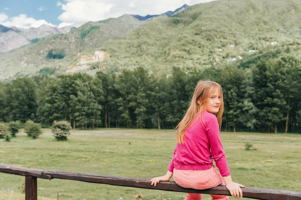 美丽的女孩在山上休息 坐在围栏上 回头看 Ovet 的肩膀 穿着粉红色的衣服 — 图库照片