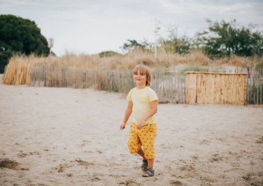 Komik çocuk çocuk deniz kum plajı üzerinde dinlenme. Genç çocuk Güney Fransa yaz tatilinin tadını çıkarıyor. Sarı t-shirt ve şort giyen çocuk